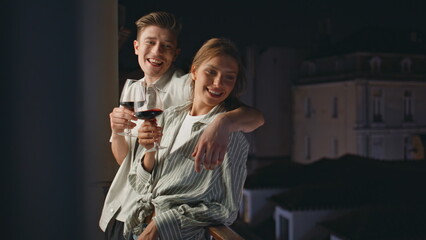 Smiling sweethearts drinking wine on balcony. Cheerful couple dating at night