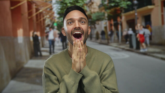 Young man surprised in an urban street setting with hands covering mouth outdoors, surrounded by bustling city life, capturing expressive emotions in a vibrant neighborhood.