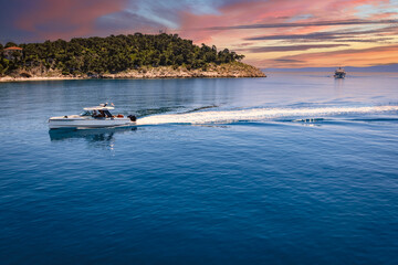 Luxury motorboat cruising on calm blue sea at sunset near a scenic Mediterranean island. Rising fuel prices make boating and tourism more expensive this summer.
