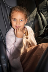 Smiling little girl sitting in a car seat wearing a soft pink sweater