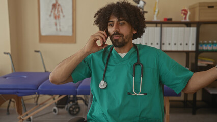 Man doctor in clinic wearing scrubs with stethoscope talking on phone and hand on forehead in visible distress; stress overload.