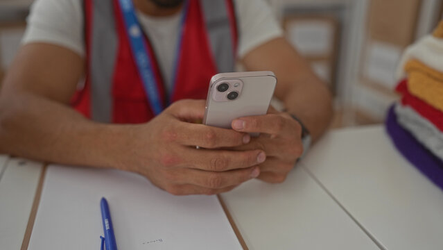 Man hands holding smartphone at donations center building, wearing volunteer vest and lanyard; community support focused.