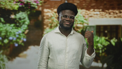 Fototapeta premium Man giving thumbs up at building entrance outdoors wearing glasses and light shirt; confidence welcome.