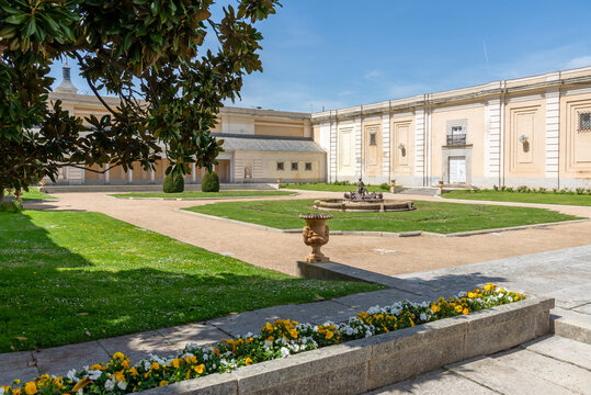 The small, symmetrical courtyard garden of El Pardo Palace featuring a central ornate stone fountain, surrounded by a gravel path and two levels of classical stone columns and archways