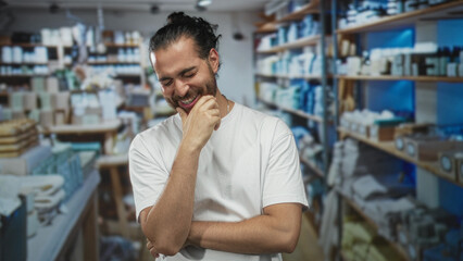 Obraz premium Man bites fingernail with hand to mouth inside home decor shop interior, smiling and slightly shy stance; playful mischief.