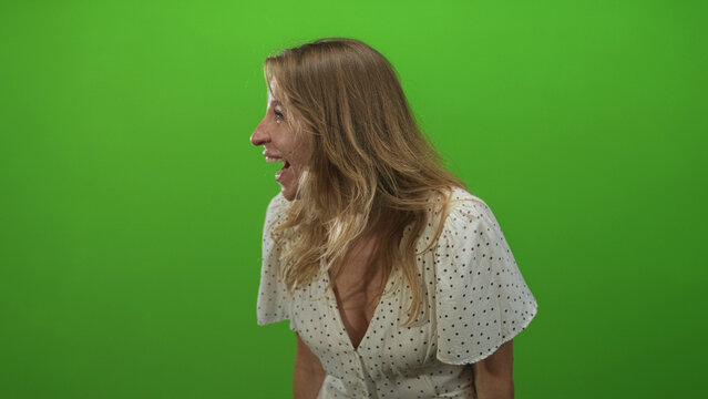 Woman laughing while turning head in green studio wearing white polka dot dress, side profile and open mouth smile; joy spontaneity.