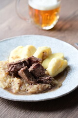 Traditional Czech dish of roasted wild boar with sauerkraut and dumplings, served on a plate in a cozy home-style setting. A hearty and flavorful meal representing authentic Czech cuisine and rustic c