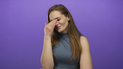 Obraz premium Woman holds hand to forehead in a purple studio setting wearing a sleeveless top with a pained expression; pain.