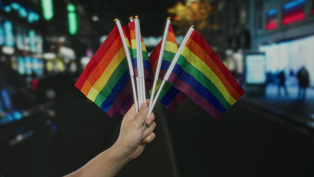 Man holding rainbow flags in a vibrant city street, highlighting lgbtq pride outdoors at night.