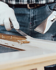 Carpenter using heat gun and wood scraper removes paint from old wooden window. Construction industry, carpentry. Restoration. 