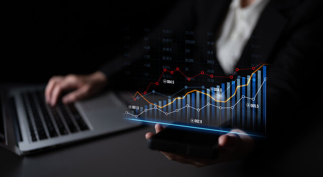 A professional focusing on business growth through data visualization, utilizing a laptop and smartphone in a modern office setup to analyze and make informed decisions. Scalp - Powered by Adobe