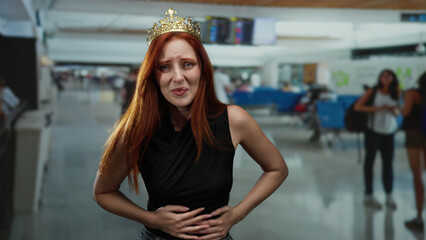 Woman with crown looking distressed at airport terminal suggesting travel discomfort amid crowded indoor setting.