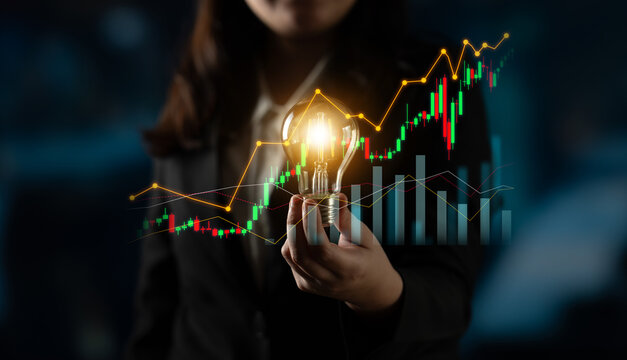 A businesswoman showcases a light bulb while standing in front of a dynamic stock chart, symbolizing creativity and innovation in finance and investment strategies. Scalp