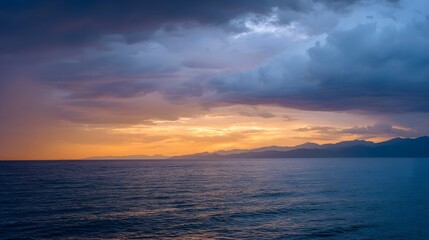 Obraz premium Dramatic stormy sunset paints the sky with vibrant orange and yellow hues over a calm ocean casting a silhouette of distant mountains