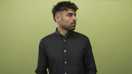 Obraz premium Young hesitant hispanic man buttoning shirt collar with both hands against light green wall in studio; fear anxiety dread worry.