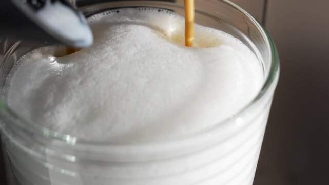 Espresso streams into a mound of milk foam. Dark coffee swirls beneath the silky top.