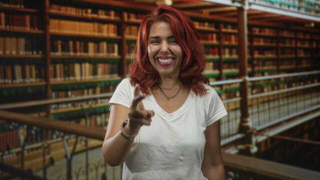 Woman with clenched fists smiling in library among tall bookshelves and railing; joy achievement success study.