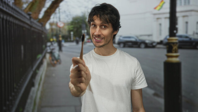 Man points a bamboo toothbrush forward with casual posture on a busy sunlit urban street corner; hygiene sustainability.