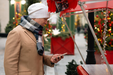 Mans buying red gift using smartphone at Christmas fairy. Xmas shopping. Side view. Holiday spirit. Close up.