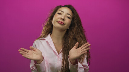 Woman face and hands shrugging with palms up in pink studio wearing light shirt and long curly...