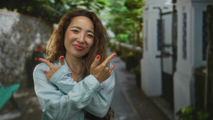 Woman with long curly hair wearing light blue shirt showing rock horns with fingers and smiling on...