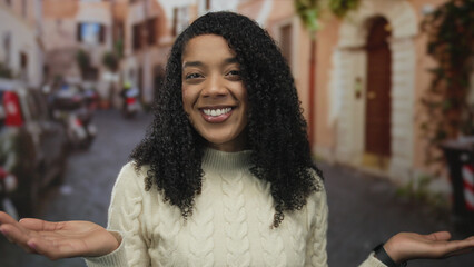Woman in white sweater smiles and holds open palms up on an old town street lined with buildings; warmth welcome.