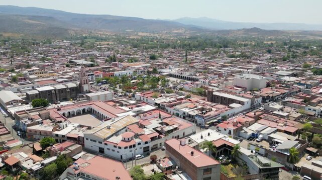Aerial reverse movement from hilltop Templo La Cruz toward Cocula's central square and buildings