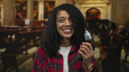African american woman holding drill with right hand and smiling in church interior; confidence empowerment.