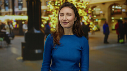 Woman smiling on city street during holiday night with bright lights and festive ambiance, young woman in blue sweater enjoying vibrant urban atmosphere outdoors.