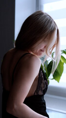Fototapeta premium A sexy beautiful woman in a black erotic negligee stands near the window in the bedroom.