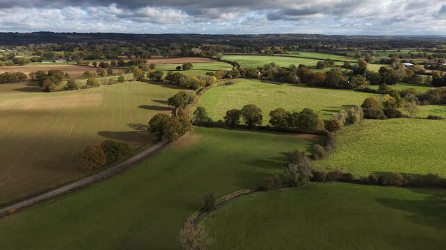 Flying above the fields in Kent, UK on a sunny day with clouds. Typical English countryside in autumn. Peaceful environment.  Agricultural fields separated by traditional hedge rows with trees.