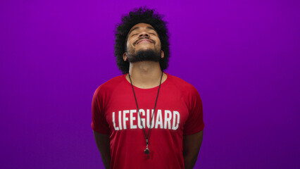 African american lifeguard man in a red shirt stands confidently against a vibrant purple wall...