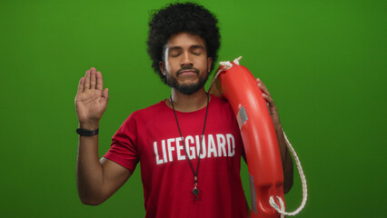 Lifeguard man in red shirt holds life preserver with oath gesture against green wall showing safety...