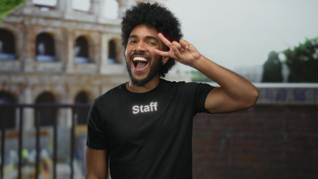 Fototapeta Smiling man in staff uniform makes victory sign at rome's iconic coliseum, showcasing a vibrant city street backdrop.