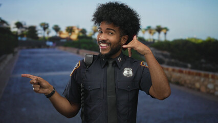 Man in police uniform outdoors gestures fun with call me sign on a sunny city street, adding a playful touch to urban enforcement.