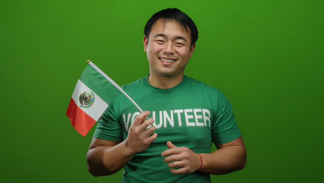Man smiling holding mexico flag wearing volunteer shirt against green background isolated cheerful young.