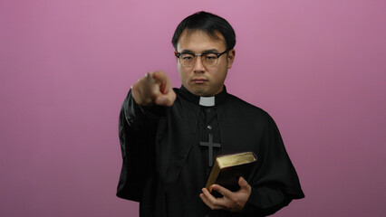 Priest holding bible pointing forward against pink background expressing authority and conviction