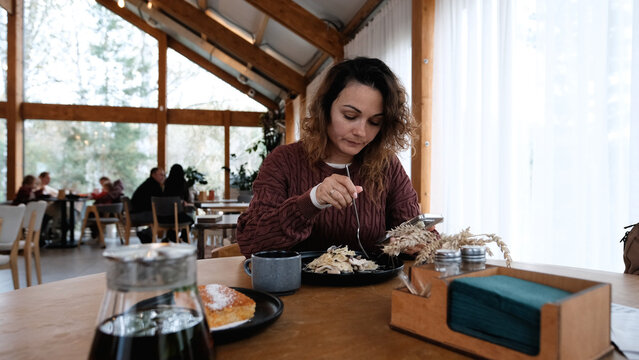 A young woman eats pasta in a restaurant and texts on her smartphone.