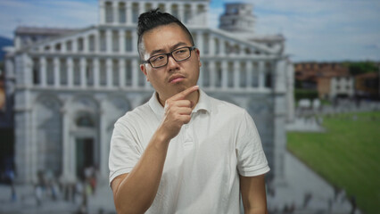 Man with glasses in a white polo points finger to the side toward a large classical building and...