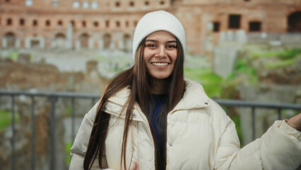 Young woman joyfully mimicking guitar playing in front of ancient roman ruins wearing a white...