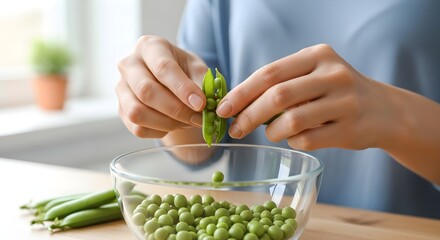 Close-up of woman shelling fresh green peas by hand into glass bowl 