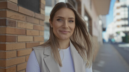 Young woman with blond hair stands smiling on a city street, showcasing a confident expression with...