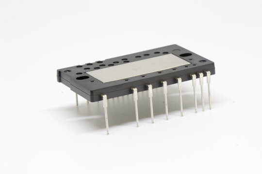 Oblique view of a black rectangular IPM power module with staggered connector pin banks and a brushed metal plate, resting on a white surface