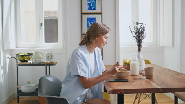 Girl answering morning call in kitchen. Relaxed woman eating breakfast talking - Powered by Adobe