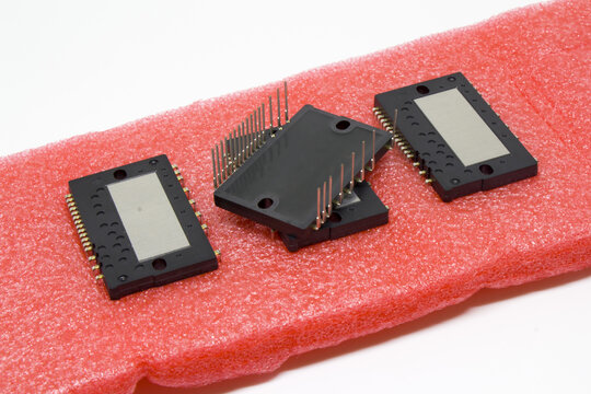 Backside view of an IPM (Intelligent Power Module) on pink ESD foam with pins facing upward, emphasizing terminals, mounting holes, and protective antistatic packaging