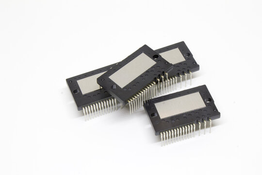 Stack of four IPM (Intelligent Power Module) devices with one placed diagonally across the others, highlighting the metal heat plate and staggered pin array, isolated on white