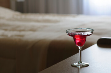 Red cocktail glass on bedside table in hotel room
