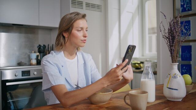 Relaxed woman using smartphone at home kitchen. Closeup surprised girl message
