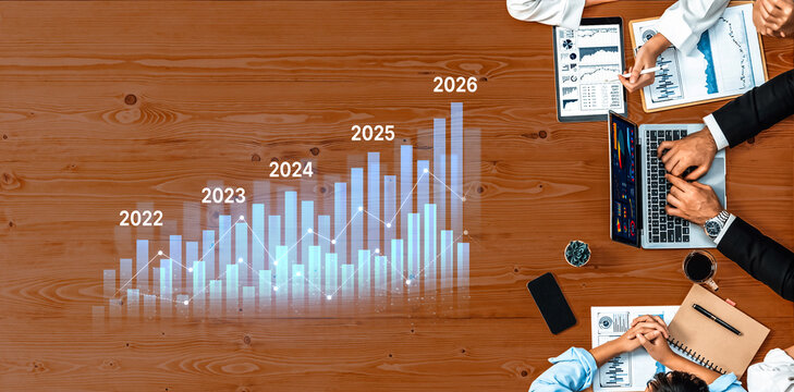 Aerial view of a business meeting with a financial analysis on a wooden table, showcasing a growth chart, laptops, and collaborative tools for strategic planning. Trope