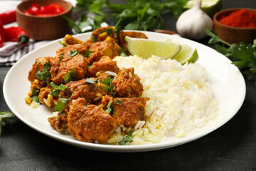 Delicious chicken tikka masala with rice, parsley and lime on dark textured table, closeup